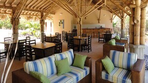 A covered outdoor dining area with bamboo structures, wicker furniture, and a kitchen in the background. - Beautiful Penthouse Condo with stunning views that occupies whole floor (Coco)