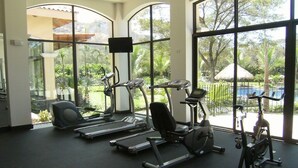 A gym with treadmills, elliptical machines, and stationary bikes, large windows with a view of greenery and a pool. - Beautiful Penthouse Condo with stunning views that occupies whole floor (Coco)