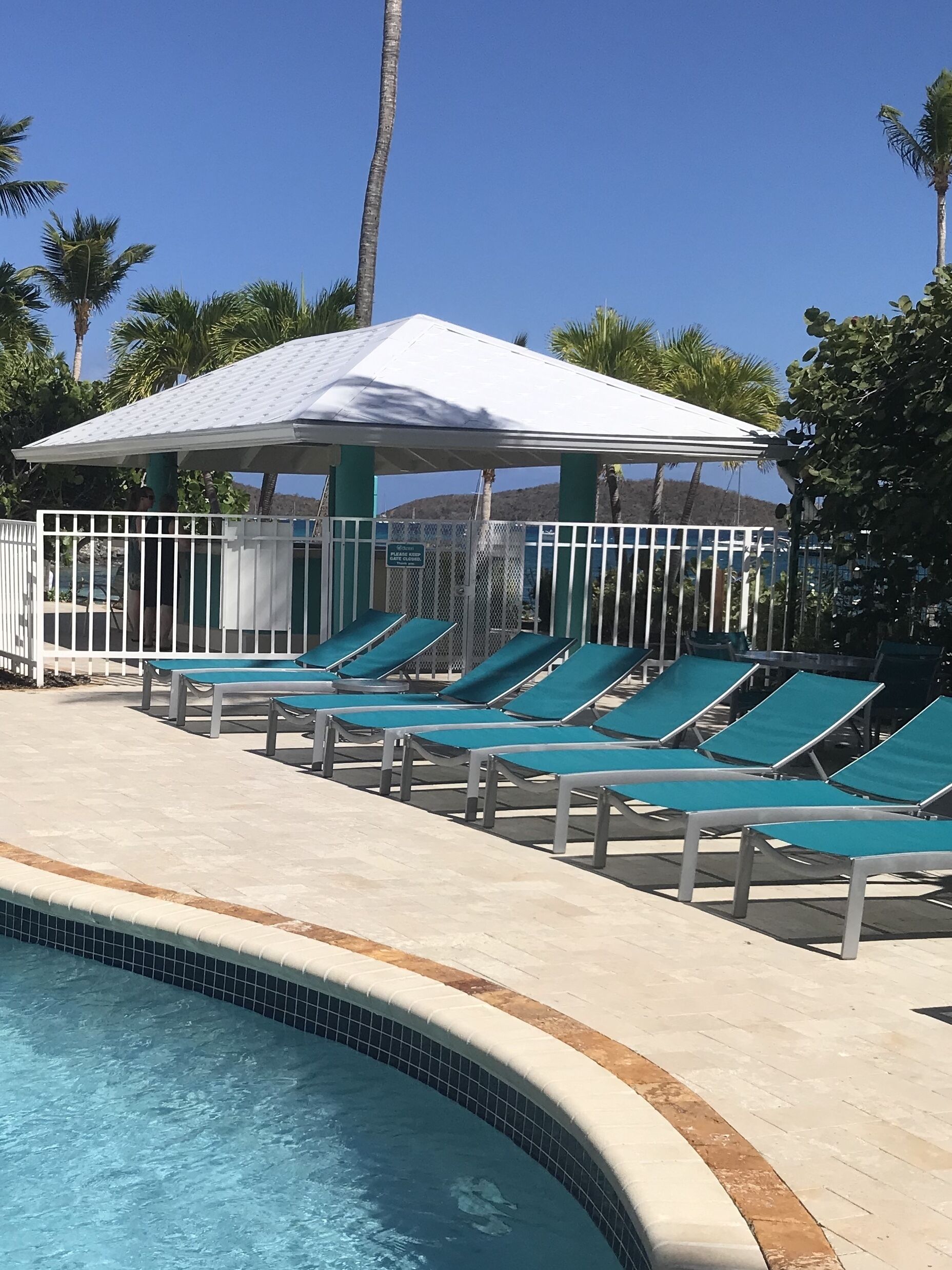 Un área junto a la piscina con sillones de descanso y una zona de estar cubierta.
