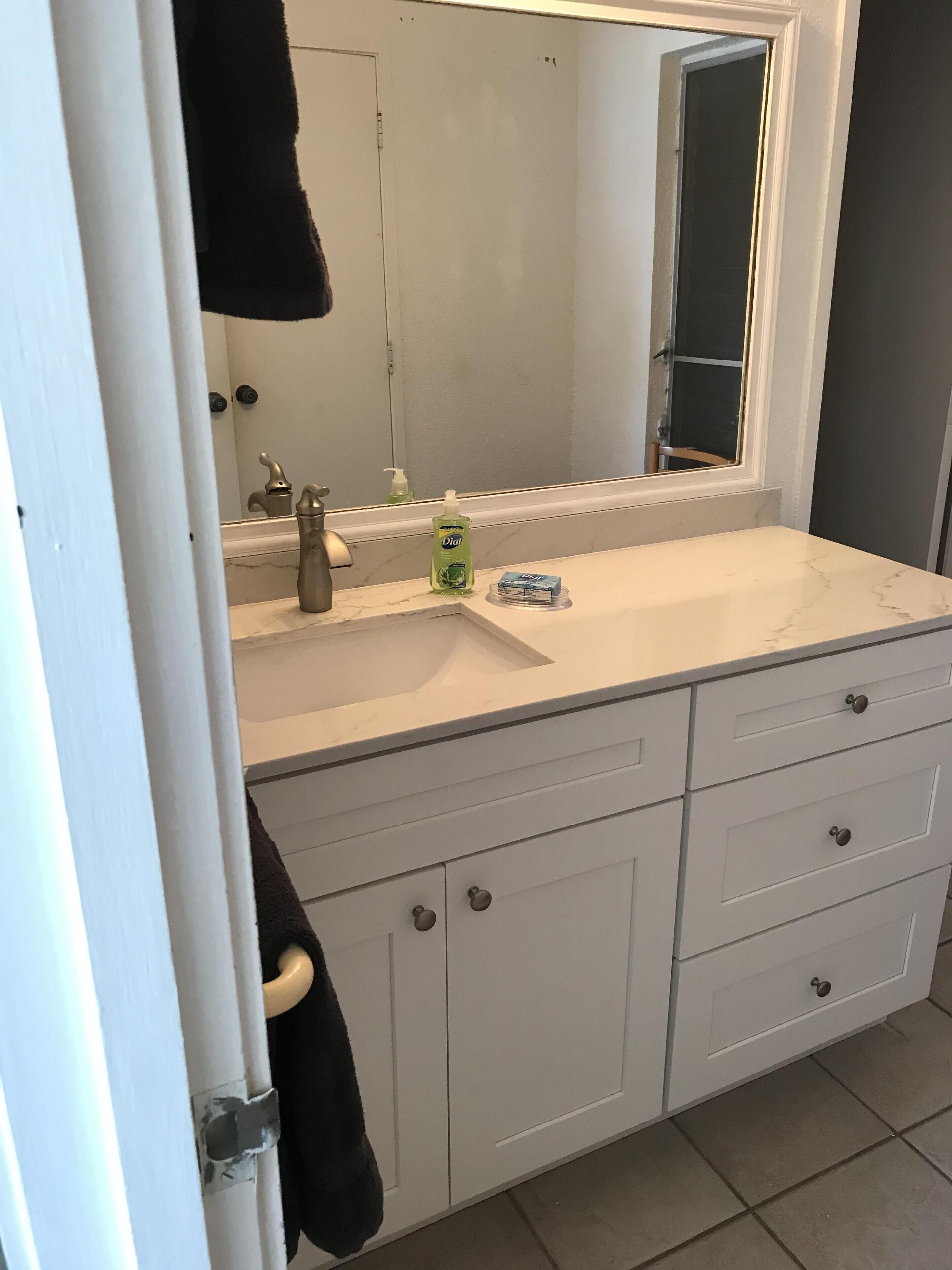 A bathroom with a white sink, a mirror, a faucet, and a bottle of Dial mouthwash. There are two drawers and a towel hanging on the door.