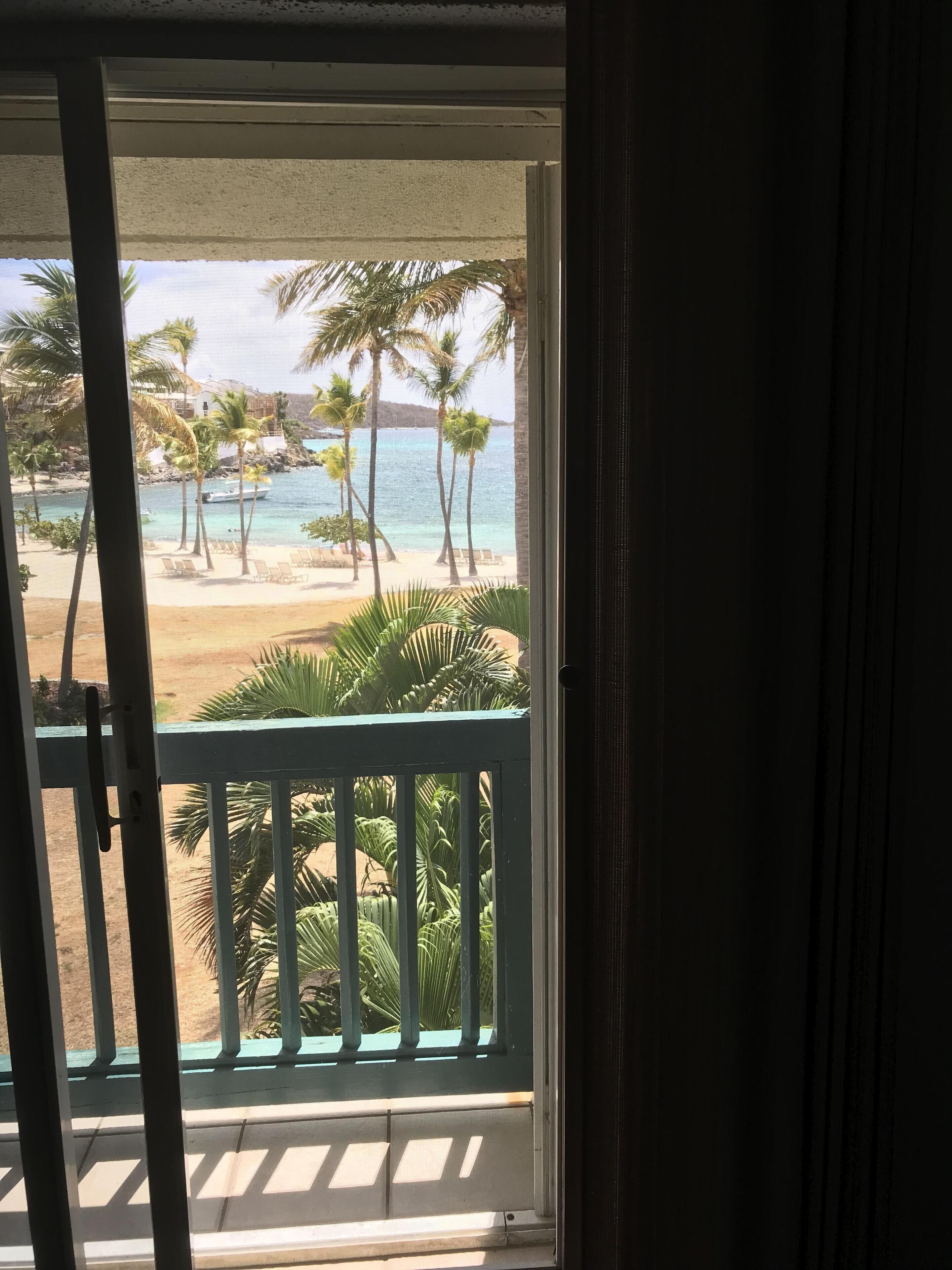 Une vue depuis un balcon donnant sur une plage bordée de palmiers, sous un ciel dégagé.