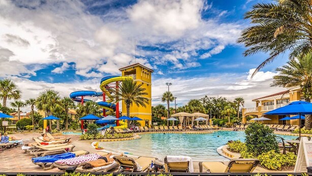 A resort pool area with a water slide, lounge chairs, and umbrellas.