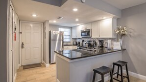 A modern kitchen with white cabinets, a stainless steel refrigerator, a microwave, and a large island with bar stools.