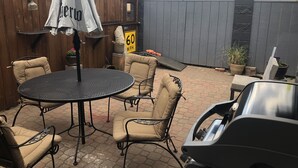 A patio area with a round metal table, beige cushioned chairs, a white umbrella, and a speed limit sign. - Unique two bedroom house in a great location in Colorado springs.   (Colorado Springs)