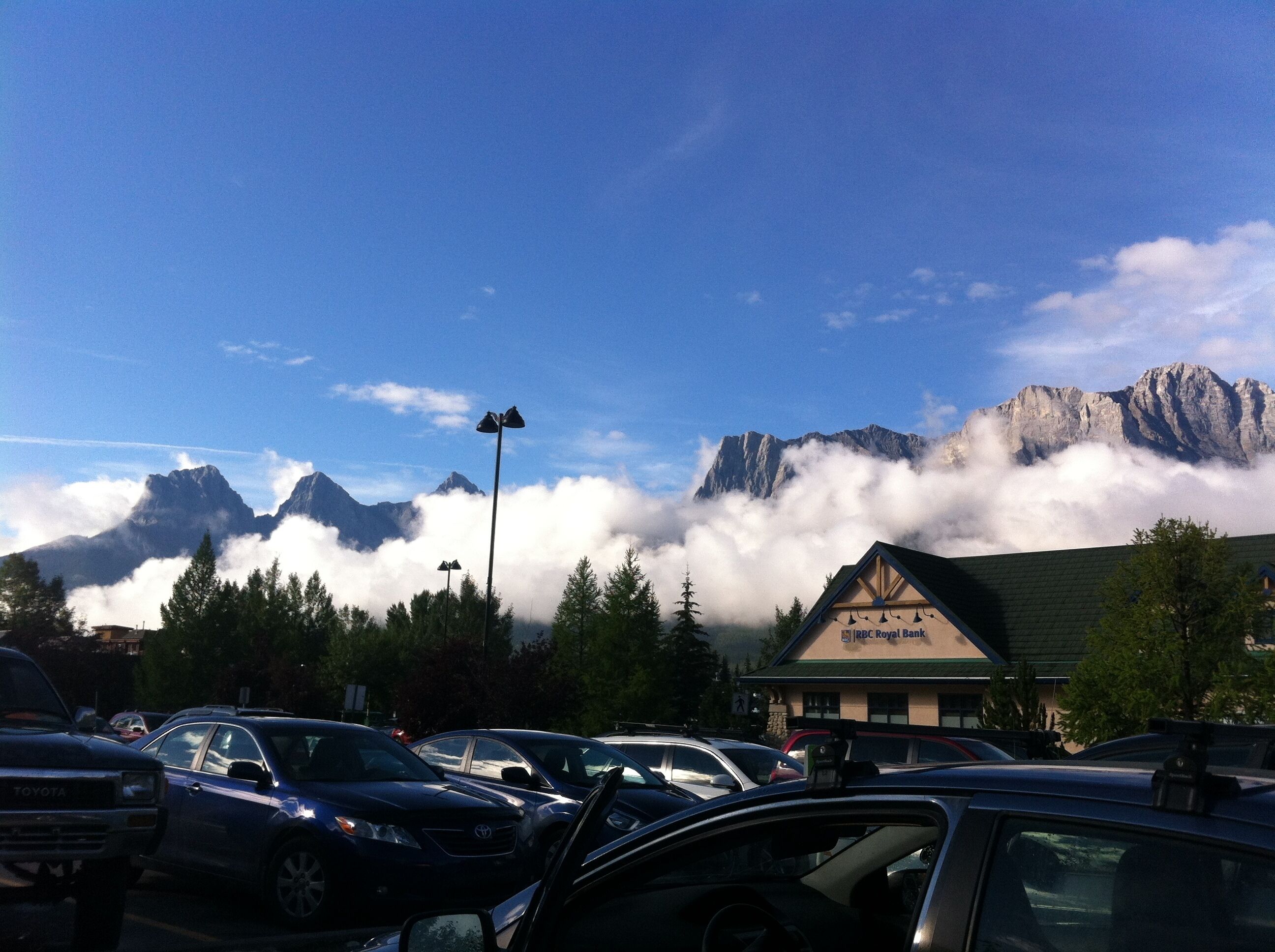 A parking lot with cars, a building labeled "UBC Royal Bank", and a mountain range with clouds in the background.