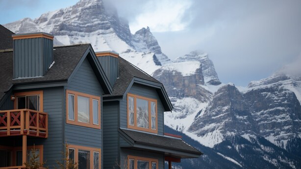 Ein zweistöckiges Haus mit Balkon vor einer Kulisse schneebedeckter Berge.