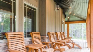 A covered porch with wooden Adirondack chairs and picnic tables, overlooking a forested area. - SPACIOUS RETREAT NEAR YELLOWSTONE. FISHING, BOATING, HIKING, ATV & SNOWMOBILING (Island Park)