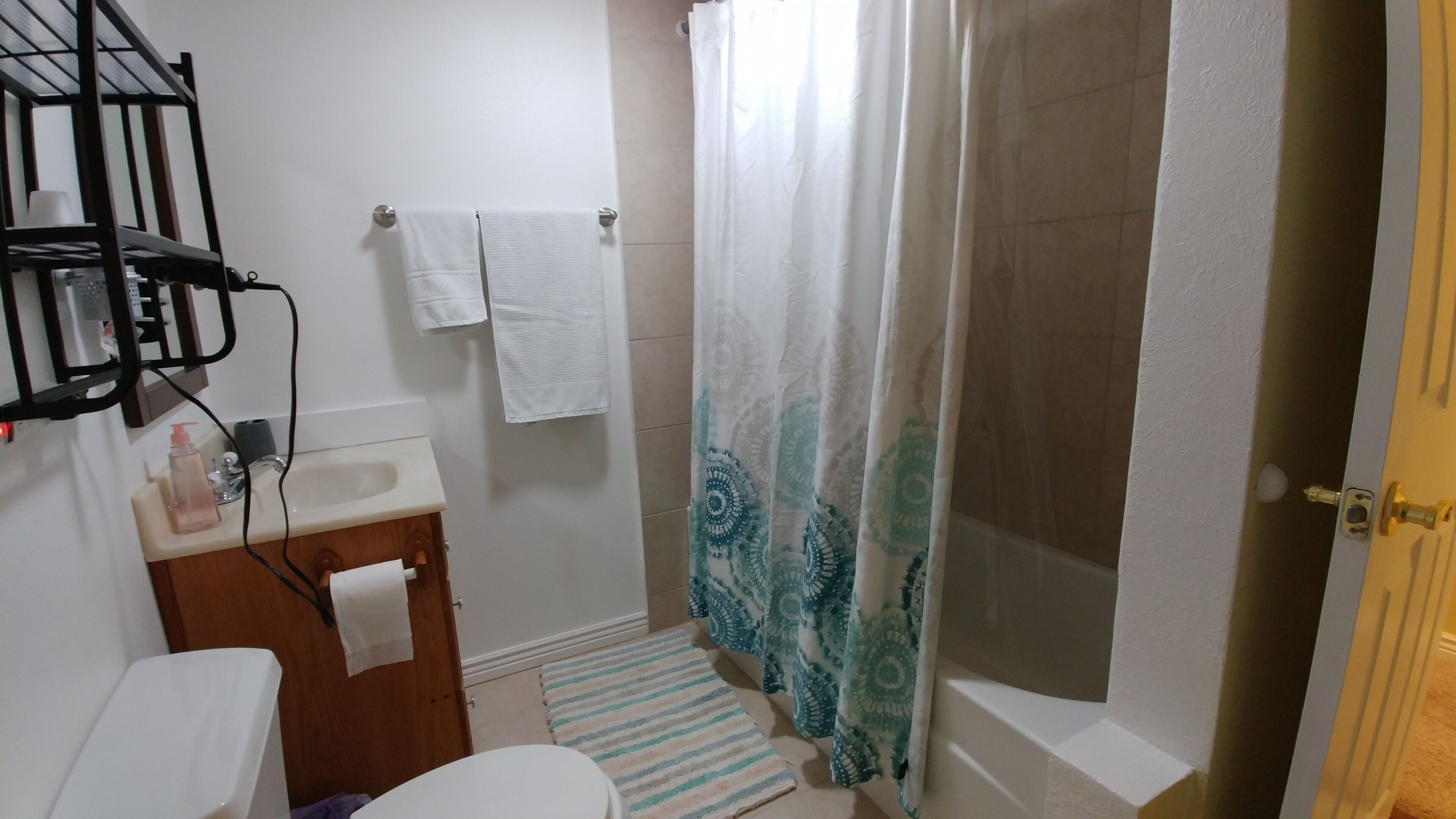 A bathroom with a toilet, sink, and shower. There is a towel rack, a shower curtain, and a striped rug.