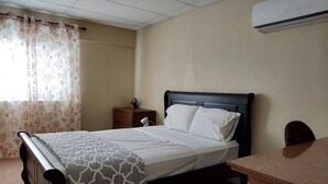 A neatly made bed with a patterned bedspread, a bedside table with a lamp, and a desk with a chair.
