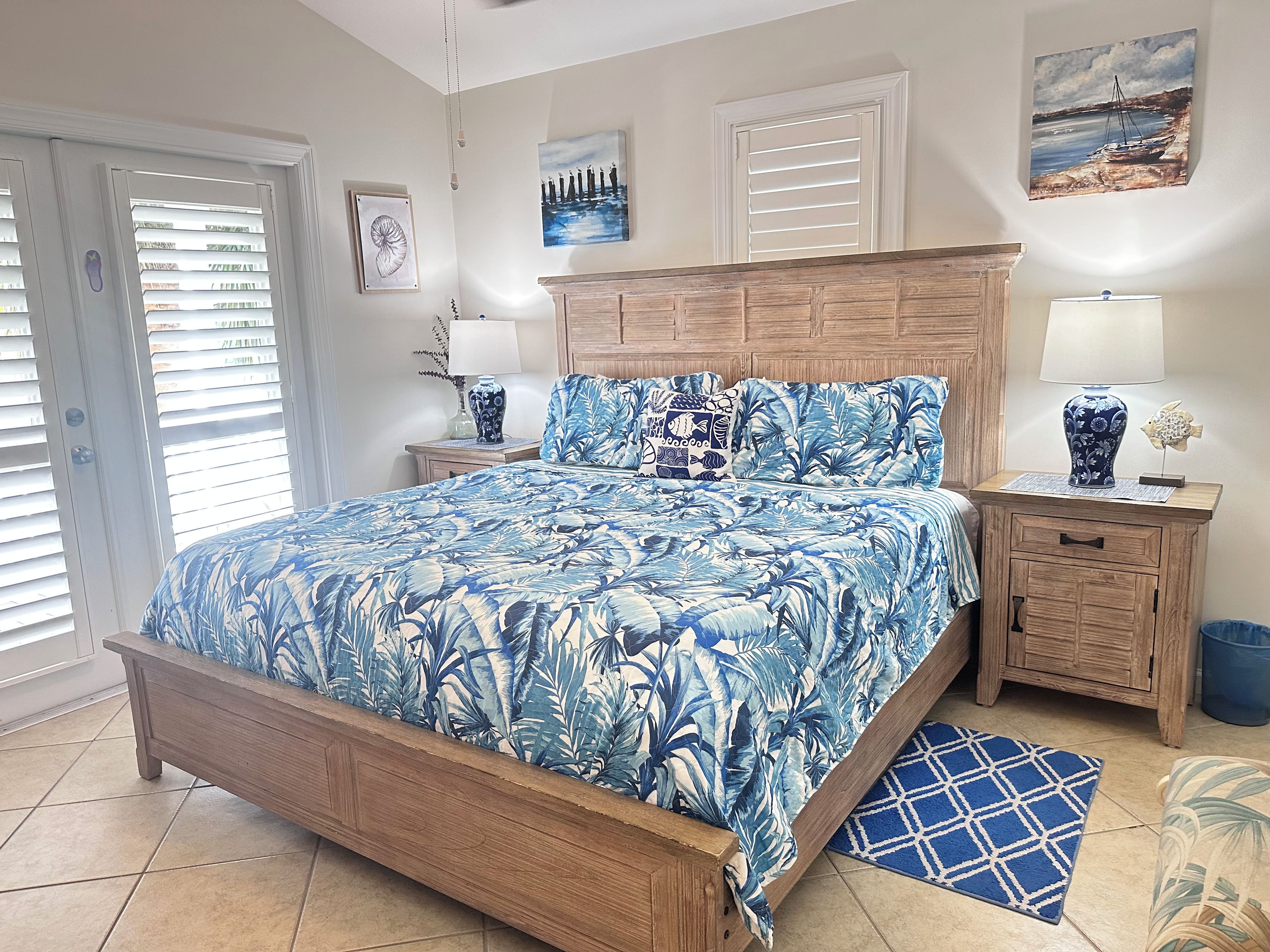 A bedroom with a bed, nightstands, a wooden headboard, and a view of the outside. - Casa Cove Beautiful Tropical 3 KING SUITES  Sleeps 8- 2 miles to beach (Stock Island)