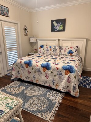 Un dormitorio con una cama cubierta con un edredón de temática marina, un plaid a juego y una alfombra tejida.