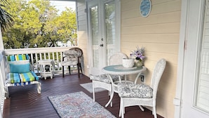 A covered porch with a ceiling fan, a white wicker table with a vase, and a colorful rug.