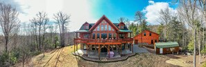 Une grande cabane en rondins dotée d’une véranda qui fait le tour de la maison et d’une autre cabane attenante.