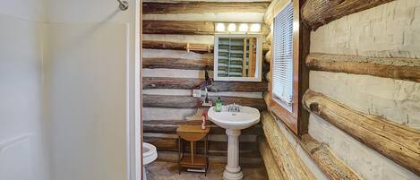 A bathroom with a wooden log wall, a pedestal sink, and a small wooden stool.