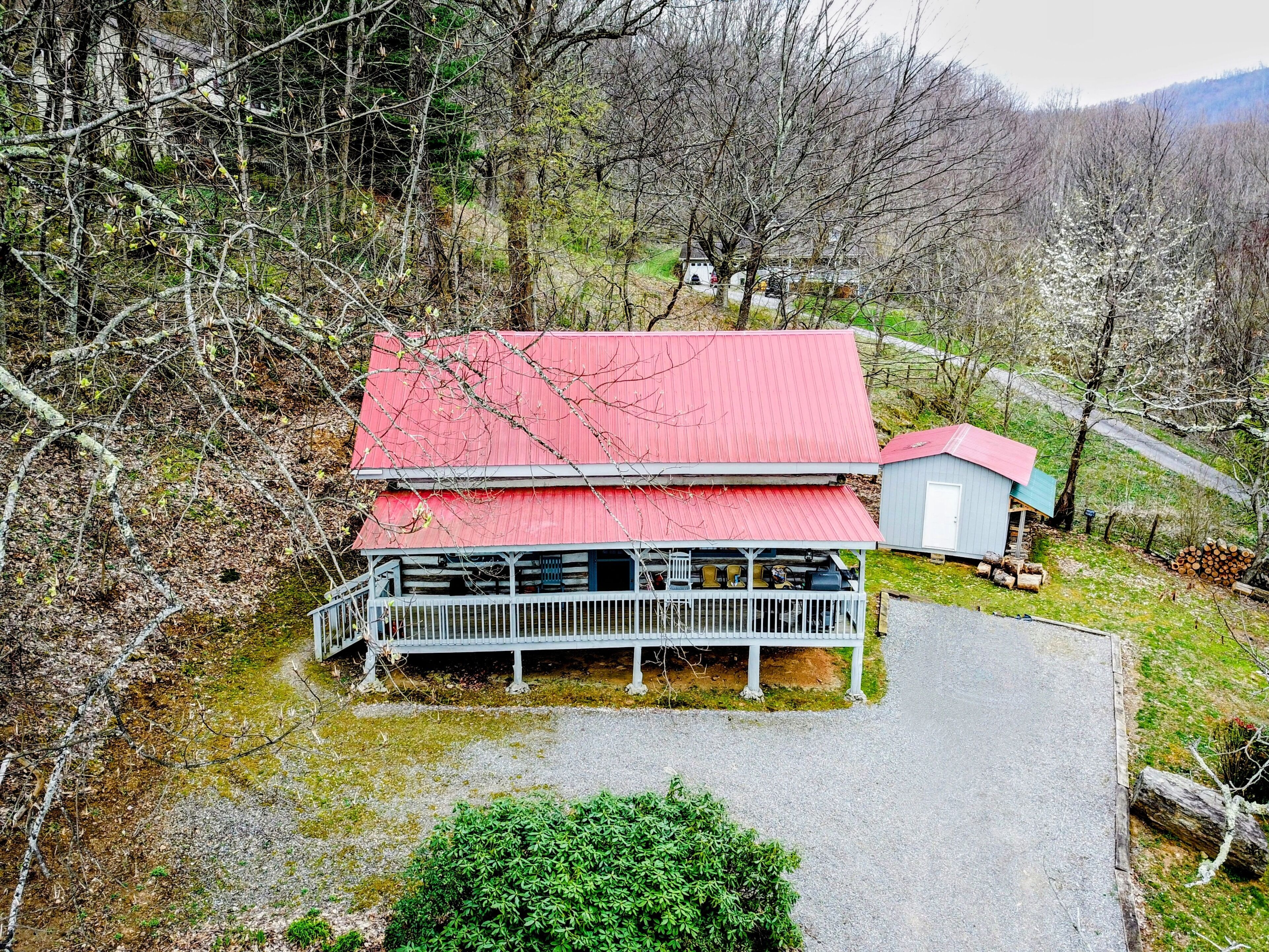 A cabin with a red roof, a porch, and a small shed.