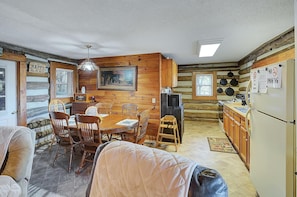 L’intérieur chaleureux d’un chalet avec une table à manger en bois, des chaises, une cheminée et un coin cuisine.