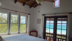 Un dormitorio con una cama grande, un ventilador de techo y vistas al océano a través de una puerta corredera.