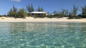 Una propiedad frente a la playa con aguas poco profundas y cristalinas, una playa arenosa y una casa con techo blanco.
