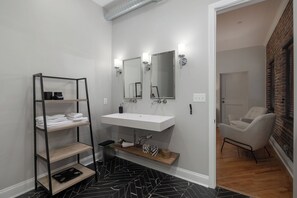 A modern bathroom with a white sink, two mirrors, and a black and white patterned floor. There is a wooden shelf with towels and a black tray. - WALK to Honky Tonks from your Private Residence Downtown (Nashville)