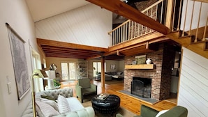 A spacious living room with a high ceiling, a fireplace, and a staircase leading to an upper level. - Gorgeous Mountain Views Retreat: Family & Nature (Hillsdale)