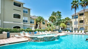 A swimming pool with lounge chairs and palm trees, surrounded by multi-story buildings.