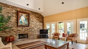 A living room with a stone wall, a fireplace, a television, two patterned armchairs, a coffee table, and a striped rug.