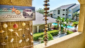 A beach-themed sign with a vintage car and starfish, a wall decorated with seashells, and a view of a pool and buildings in the background.