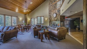 A spacious living room with leather sofas, a stone fireplace, and large windows offering views of the outdoors. - Ski in / ski out family friendly condo w/access to pool, hot tub & game room (Winter Park)