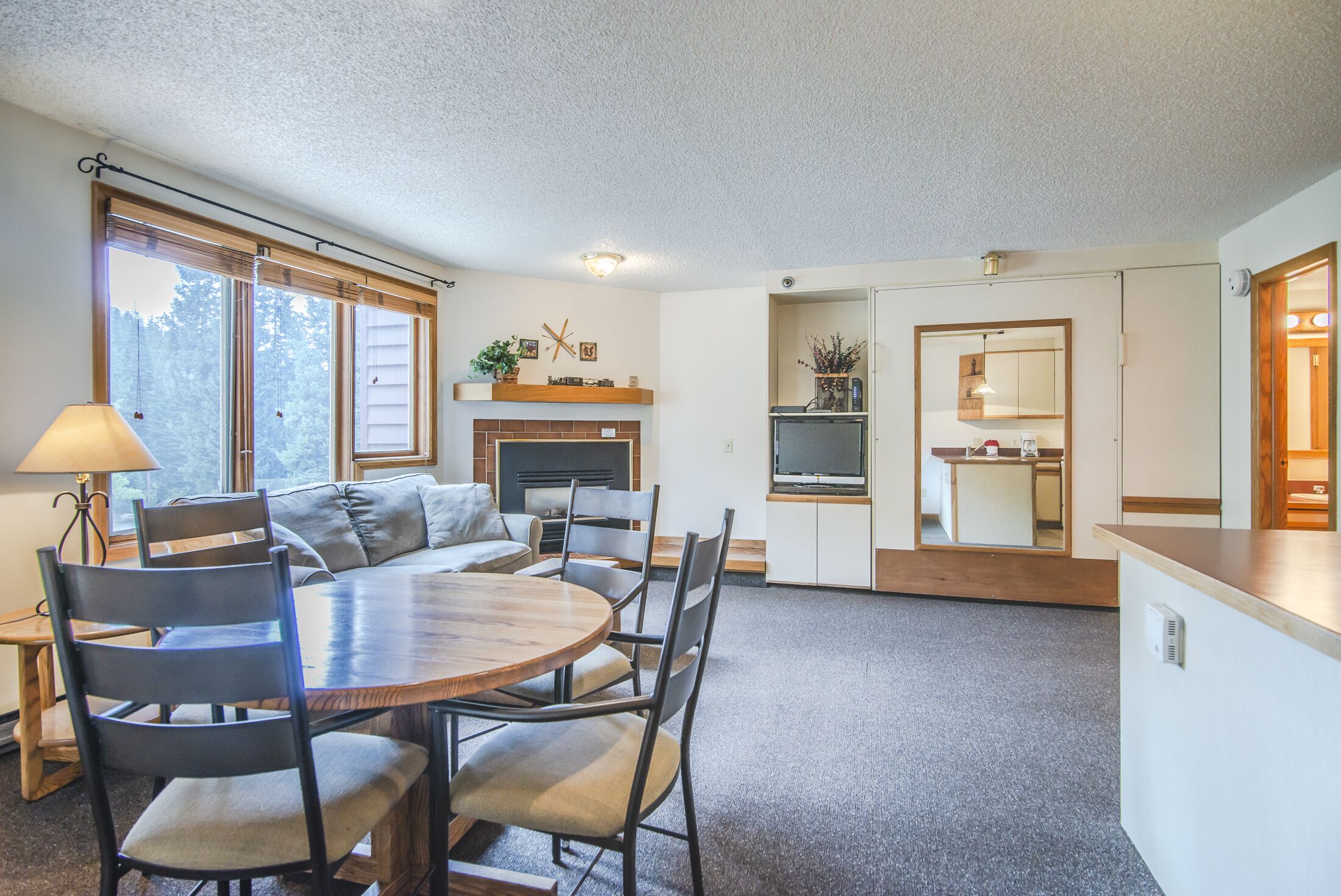 A cozy living area with a fireplace, a dining table with chairs, a sofa, and a kitchen area visible through an open door.