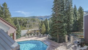 A swimming pool with a deck area, surrounded by tall trees and a mountainous backdrop. - Ski in / ski out family friendly condo w/access to pool, hot tub & game room (Winter Park)