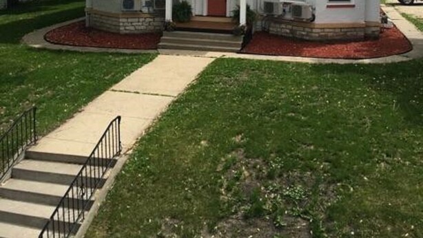 A two-story building with a central entrance, a small porch, and a circular window above the door. - Day Street Suites. Historic Phelps Mansion.  Main Level Suite #2 (Decorah)