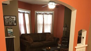 A living room with a sofa, a coffee table, and a dining area with a red table and chairs. - Day Street Suites. Historic Phelps Mansion.  Main Level Suite #2 (Decorah)