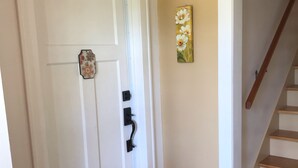 A white door with a doormat, a black doorbell, and a wall-mounted flower painting. - Day Street Suites. Historic Phelps Mansion.  Main Level Suite #2 (Decorah)