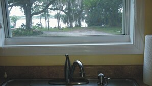 Un lavamanos de cocina con una ventana arriba, con vistas a una carretera y árboles.