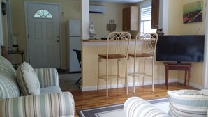 Una sala con sofás a rayas, una zona de cocina con un refrigerador y un taburete de bar.