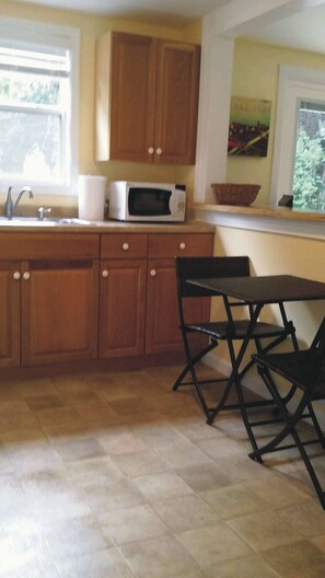 A kitchen with wooden cabinets, a microwave, a sink, and a dining area with a table and chairs. - Riverfront One Bedroom Fishing Cottage w/ boat dock-Summer Specials!! (Sebastian)