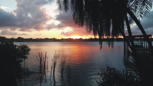 A sunset over a calm lake with a dock and palm trees.