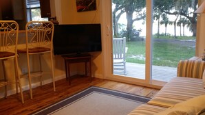 Una sala de estar con televisor, dos sillones, un sofá y un ventanal corredera que da a una terraza.