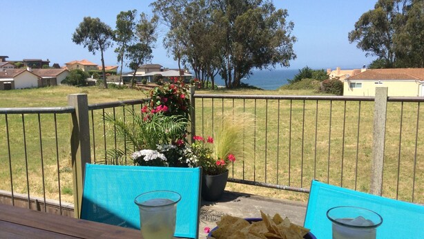 Un balcón con vista al mar, una mesa con un bol de patatas y dos vasos de un líquido transparente.