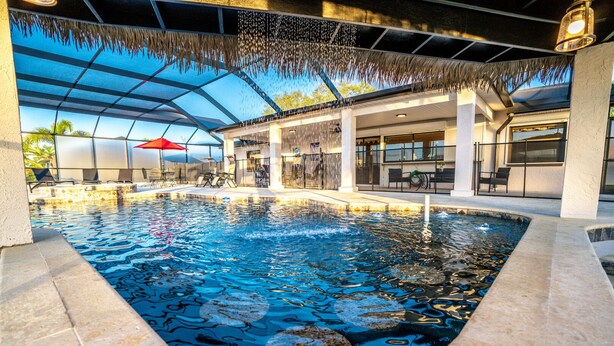 An indoor swimming pool with clear water, surrounded by lounge chairs and umbrellas, and a covered seating area with tables and chairs.