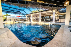 Piscina interior com água cristalina, rodeada por espreguiçadeiras e guarda-sóis, e área de estar coberta com mesas e cadeiras.