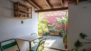 En lille terrasse med et bord, stole, en kurveshelf og potteplanter.