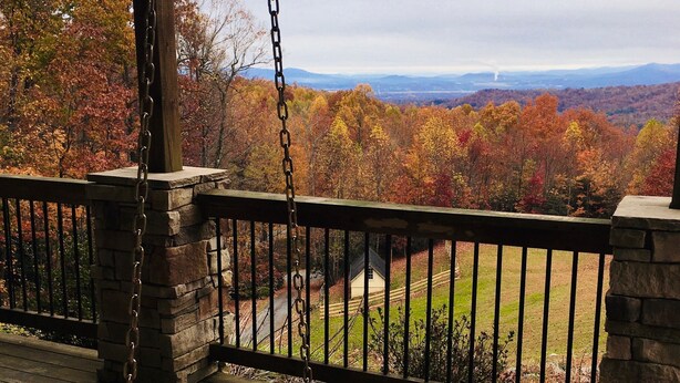 A wooden deck with a swing, stone balustrade, and a view of autumn foliage and distant mountains. - Beautiful Long Range Mountain Views, Minutes from Downtown Hendersonville, NC (Hendersonville)