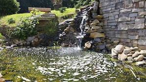 A pond with a waterfall, surrounded by stone walls and greenery. - Beautiful Long Range Mountain Views, Minutes from Downtown Hendersonville, NC (Hendersonville)