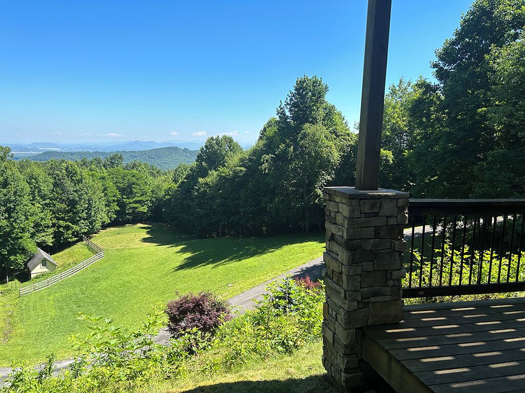 A stone pillar with a bench, overlooking a green field and distant mountains.