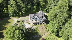 A large, two-story house surrounded by dense forest, with a driveway and a small parking area visible. - Beautiful Long Range Mountain Views, Minutes from Downtown Hendersonville, NC (Hendersonville)