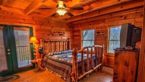 A log cabin bedroom with a wooden bed, a television, and a ceiling fan.