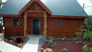 A log cabin with a metal roof, a front door, and a small porch area.
