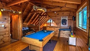 A wooden cabin with a pool table, a bunk bed, and a poster on the wall.