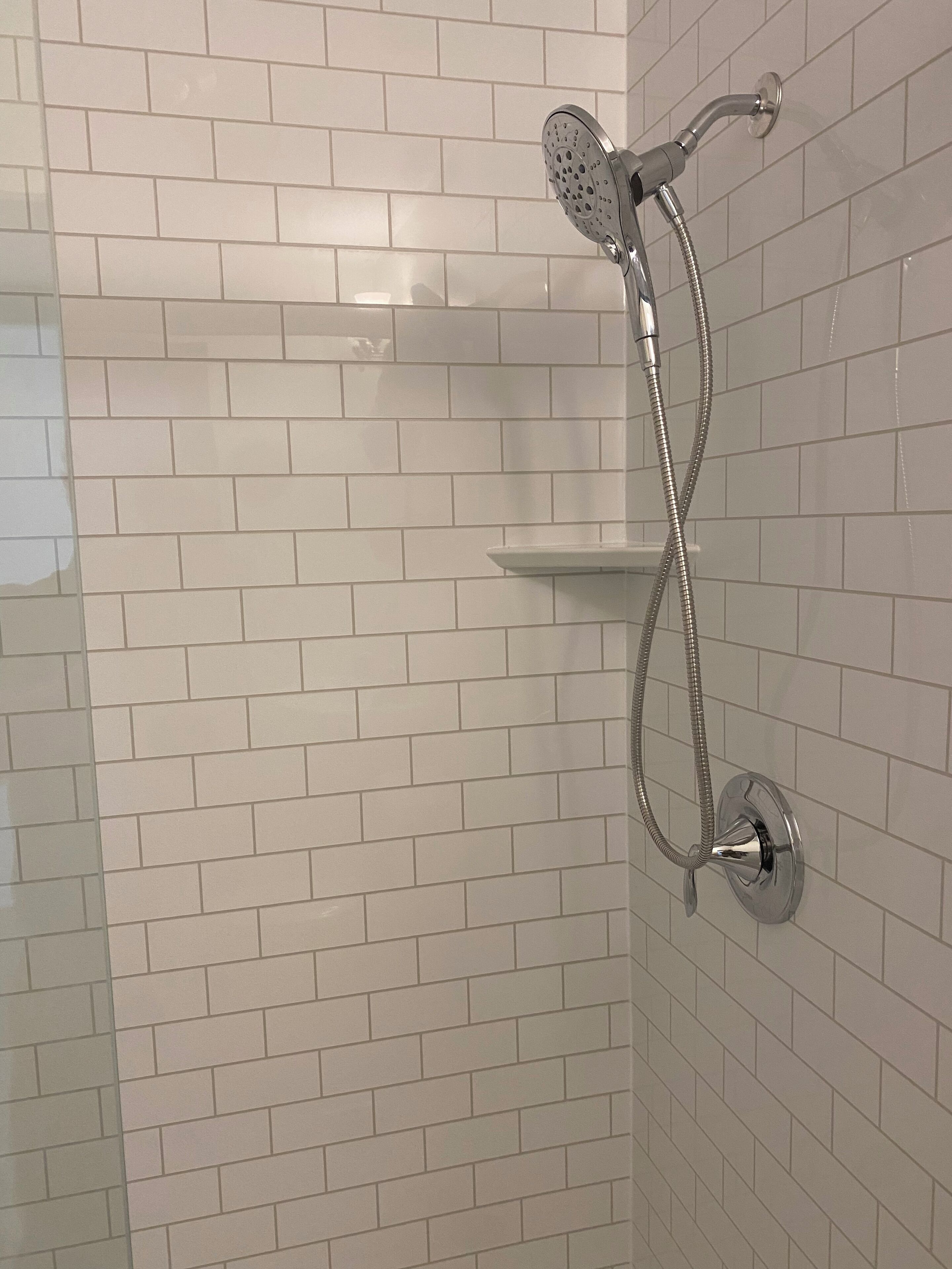 Une douche équipée d’un pommeau de douche à main et d’un flexible, le tout fixé sur un mur carrelé.